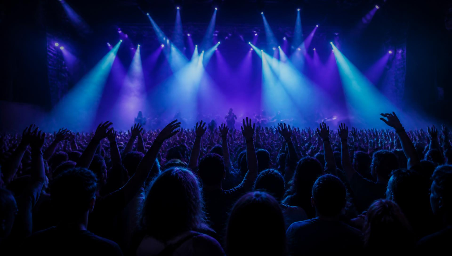 Concert crowd with raised hands under violet and cyan stage lights